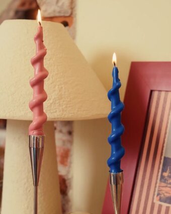 Velas trançadas rosa e azul acesas sobre aparador